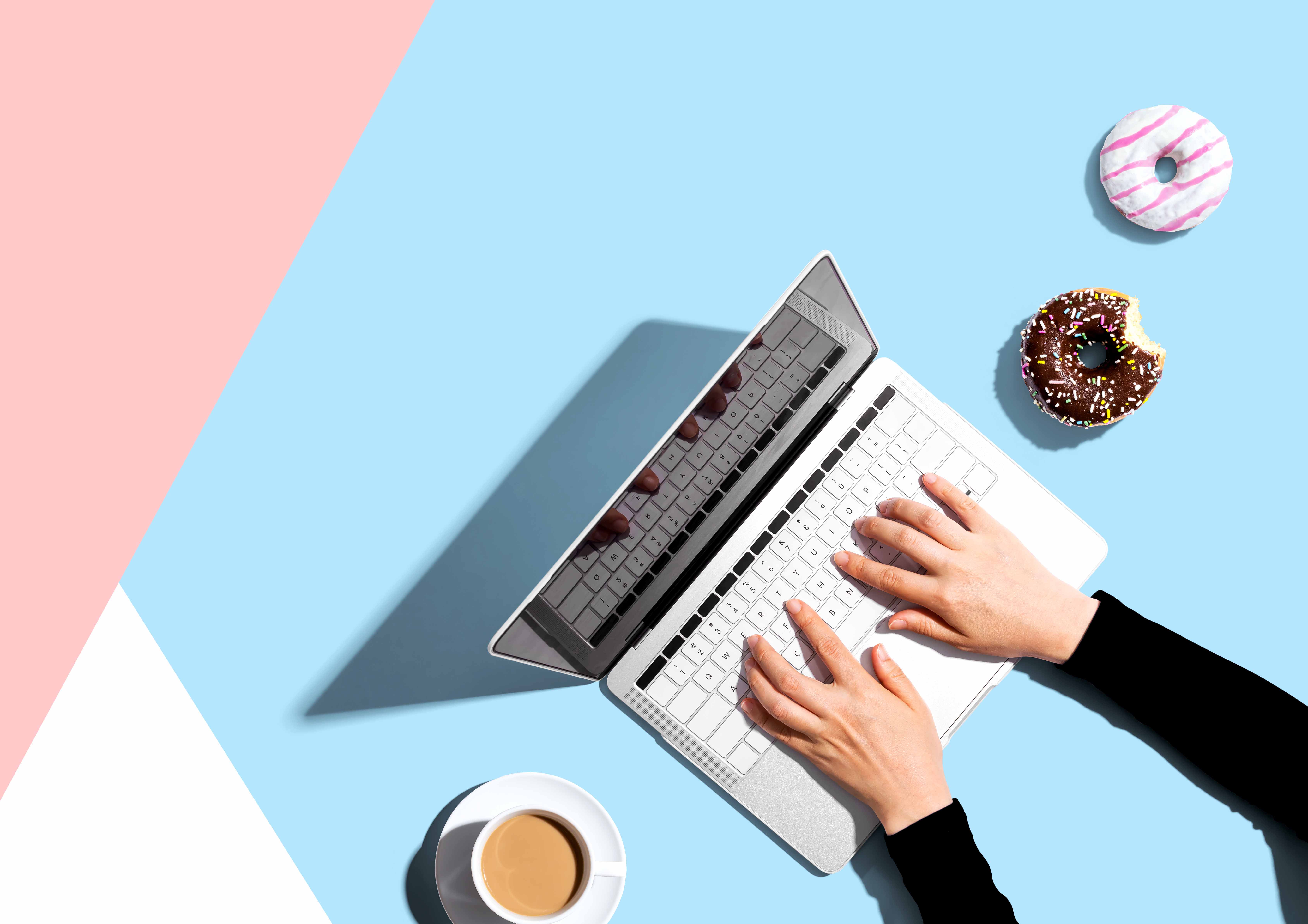 Person using a laptop computer with a donut and a cup of coffee